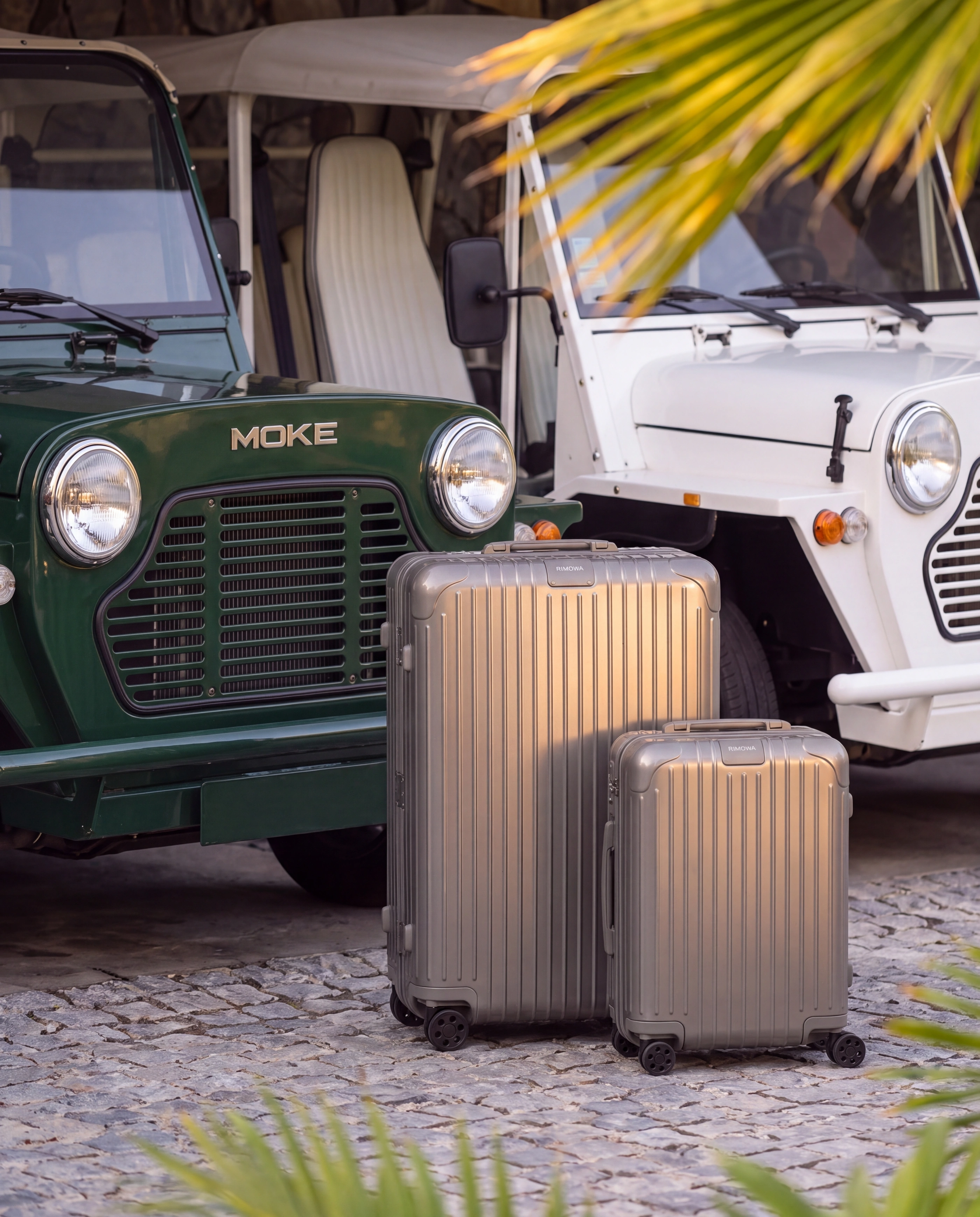 Two suitcases on the cobbles in front of a green Moke and a white one